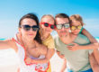 Un couple et leurs deux enfants prennent un selfie sur plage, heureux d'avoir économiser sur le montant de leur assurance voyage.