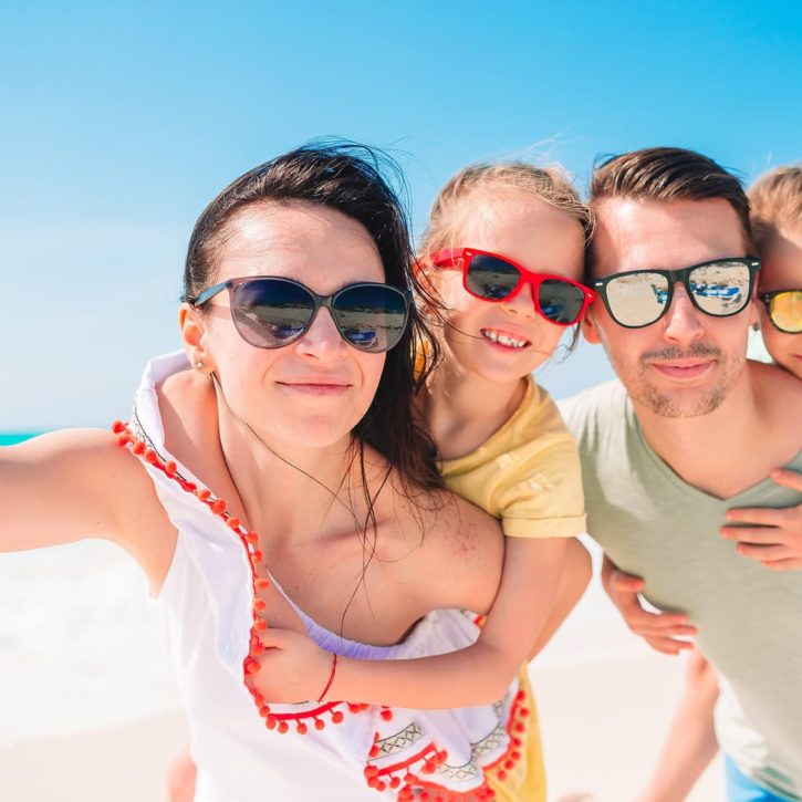 Aurrance voyage annuelle pour faire des économies Un couple et leurs deux enfants prennent un selfie sur plage, heureux d'avoir économiser sur le montant de leur assurance voyage.
